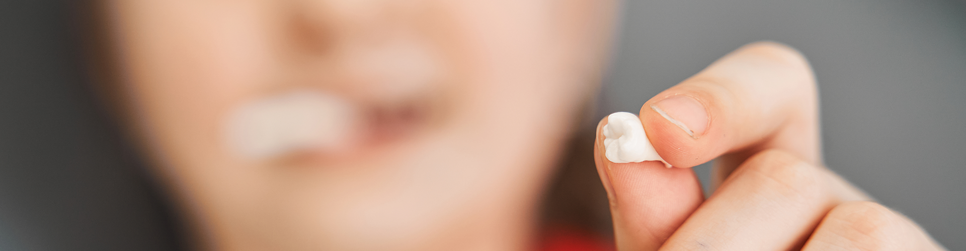 hand holding extracted tooth with blurred person in background